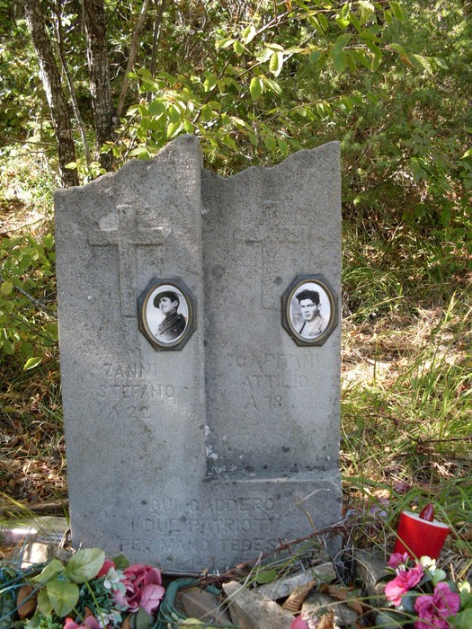 Cippo commemorativo di Zanni e Capitani, con foto e fiori, in un contesto naturale.