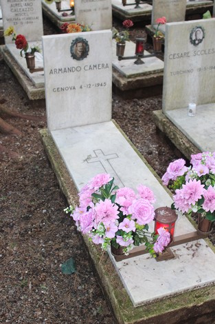 Tombe bianche decorate con fiori e candele, dedicate ai caduti per la Libertà. Atmosfera commemorativa e di rispetto.