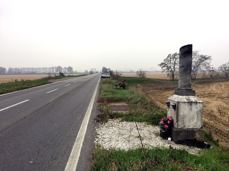 Cippo a Camussoni lungo una strada di campagna, circondato da un paesaggio rurale nebbioso.