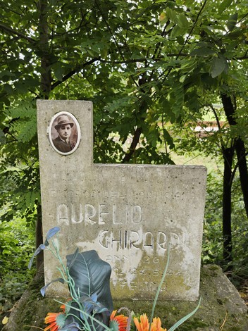 Cippo memoriale dedicato a Aurelio Ghirardi, ubicato in un contesto naturale, circondato da vegetazione.