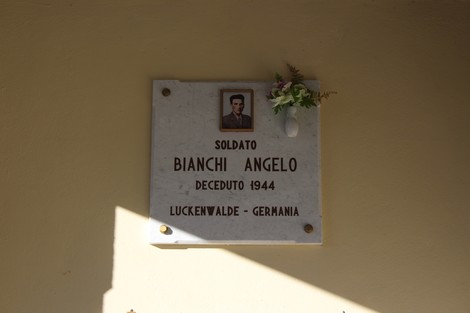 Lapide commemorativa di un soldato al Cimitero di Cornalba, con decorazioni floreali e un ritratto.