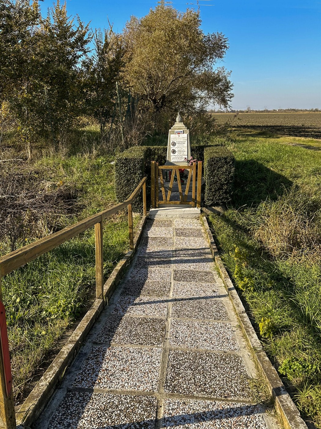 Sentiero panoramico che conduce al cippo commemorativo ai Fornasari, circondato da natura e campi aperti.
