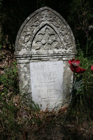 Cippo in memoria di Maria Fini, deceduta nel 1944, circondato da vegetazione.