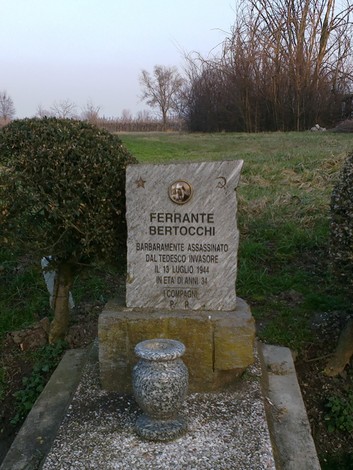 Cippo commemorativo dedicato a Ferrante Bertocchi, vittima della guerra, situato in un paesaggio rurale.