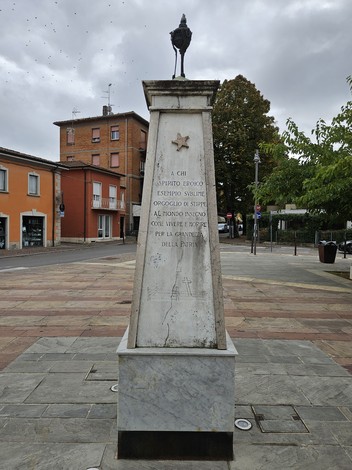 Monumento ai Partigiani, con iscrizioni commemorative e una stella, circondato da un contesto urbano.
