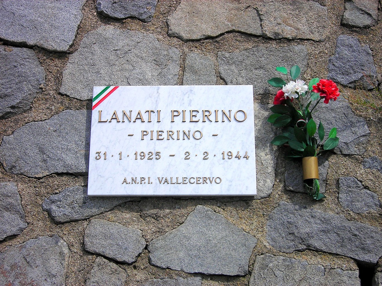 Lapide commemorativa di Pierino Lanati, con fiori e stendardi tricolori, in memoria della sua vita.