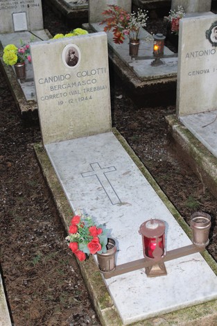 Tomba con epigrafe di Candido Colotti, decorata con fiori e lanterne, in un cimitero commemorativo.