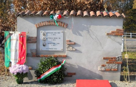 Monumento commemorativo dedicato a Morecchio, Vettorello e Sereno, con decorazioni tricolore e fiori.