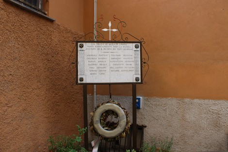 Lapide commemorativa con dedica ai caduti della Croce Bianca, decorata da una corona di fiori.