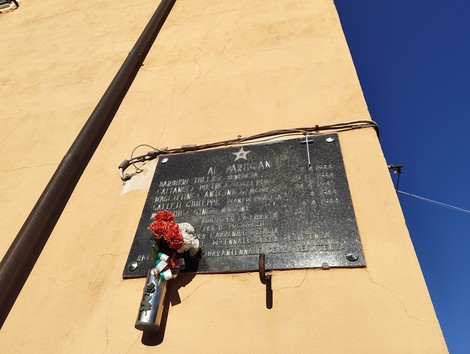 Lapide commemorativa dedicata ai caduti per la Libertà a San Quirico, adornata con fiori e un cero.