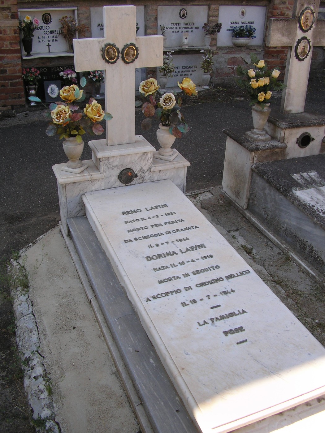 Sepolcro dei Lapini con croce, fiori e iscrizioni commemorative in marmo bianco. Un luogo di memoria e riposo.