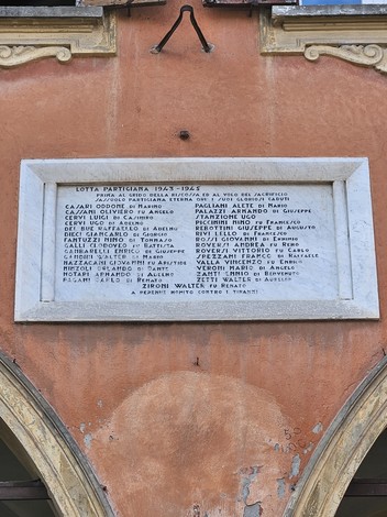 Lapide commemorativa dedicata ai partigiani caduti, affissa su un edificio storico.