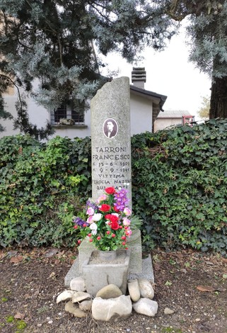 Cippo commemorativo di Francesco Tarroni, decorato con fiori e collocato in un contesto verde.