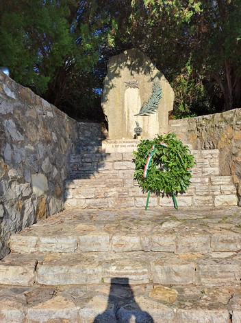 Lapide commemorativa ai caduti di Massaciuccoli, con corona di alloro e natura circostante.