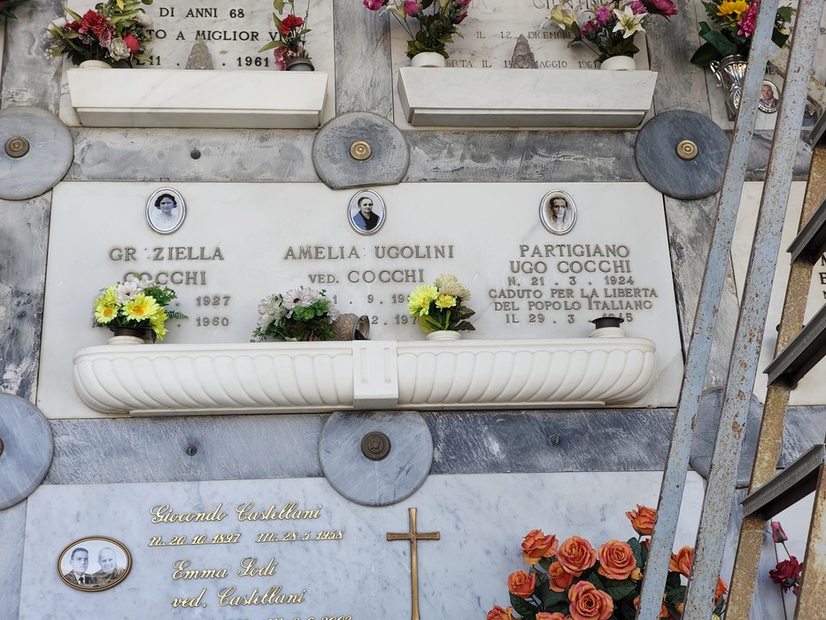 Loculi cimiteriali in marmo con foto ovali, iscrizioni e fiori, tra cui quello di un partigiano.