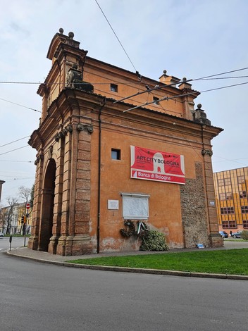 Lapide commemorativa posizionata su un edificio storico di Bologna, con architettura elegante e dettagli artistici.