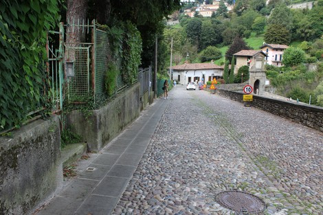 Stradina acciottolata a Sirtoli, circondata da edifici storici e vegetazione lussureggiante.