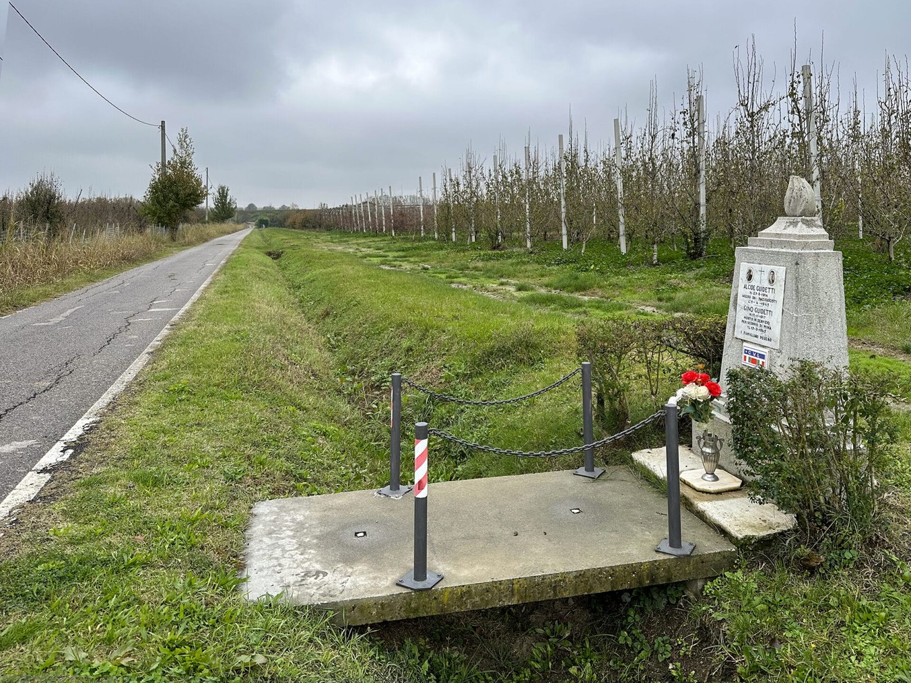Cippo commemorativo ai Guidetti, immerso in un paesaggio rurale, con fiori e un sentiero a fianco.