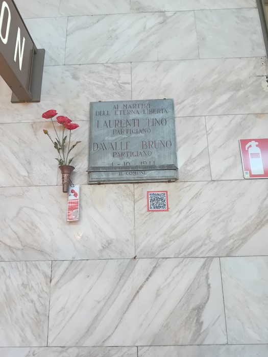Lapide commemorativa dedicata ai partigiani Laurenti e Davalle, con fiori freschi e decorazioni.