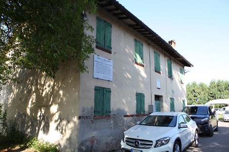 Lapide a Degli Esposti su un edificio storico con finestre verde scuro e automobile parcheggiata.