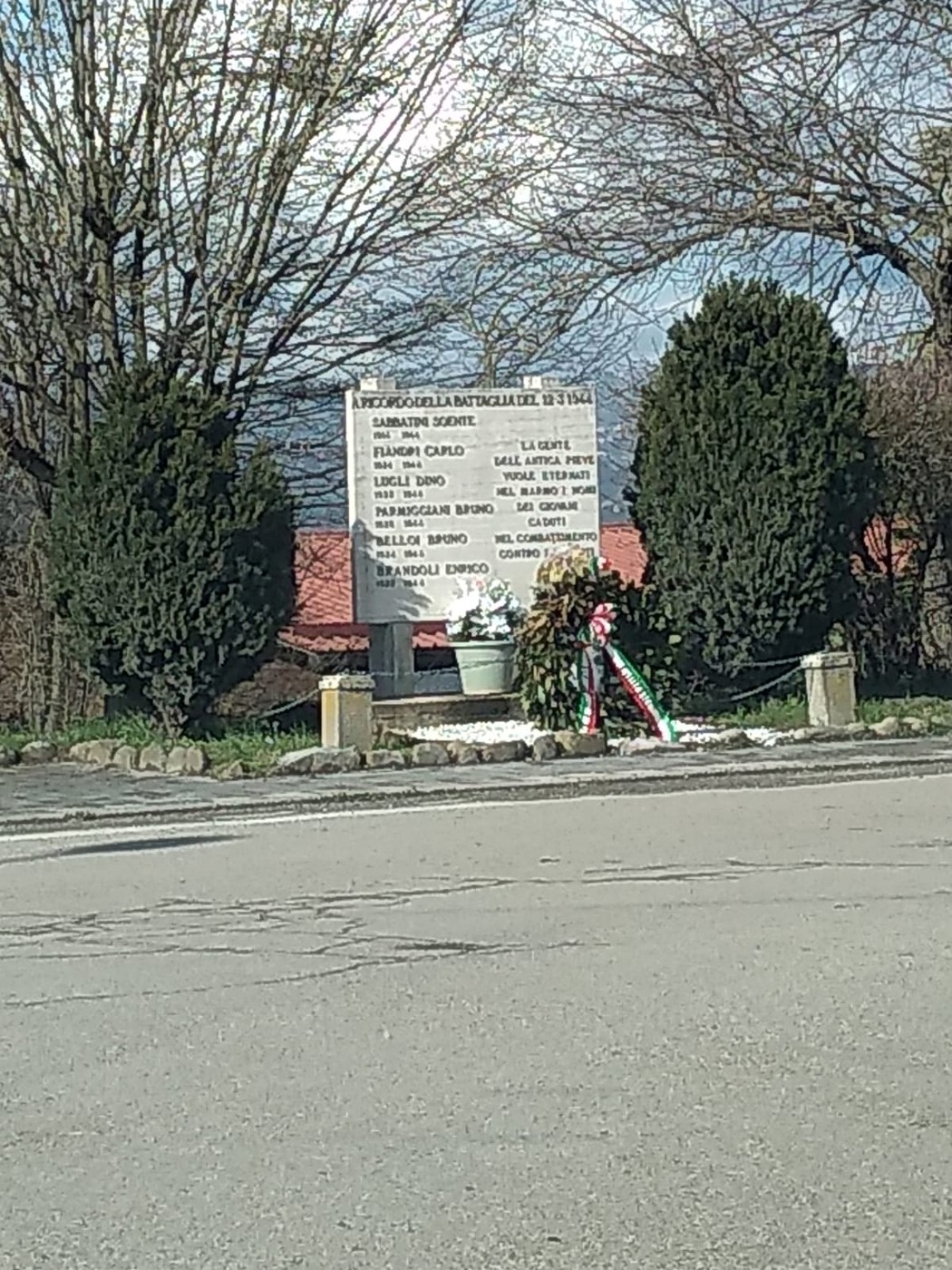 Monumento commemorativo della battaglia di Pieve di Trebbio, circondato da alberi e decorato con fiori.